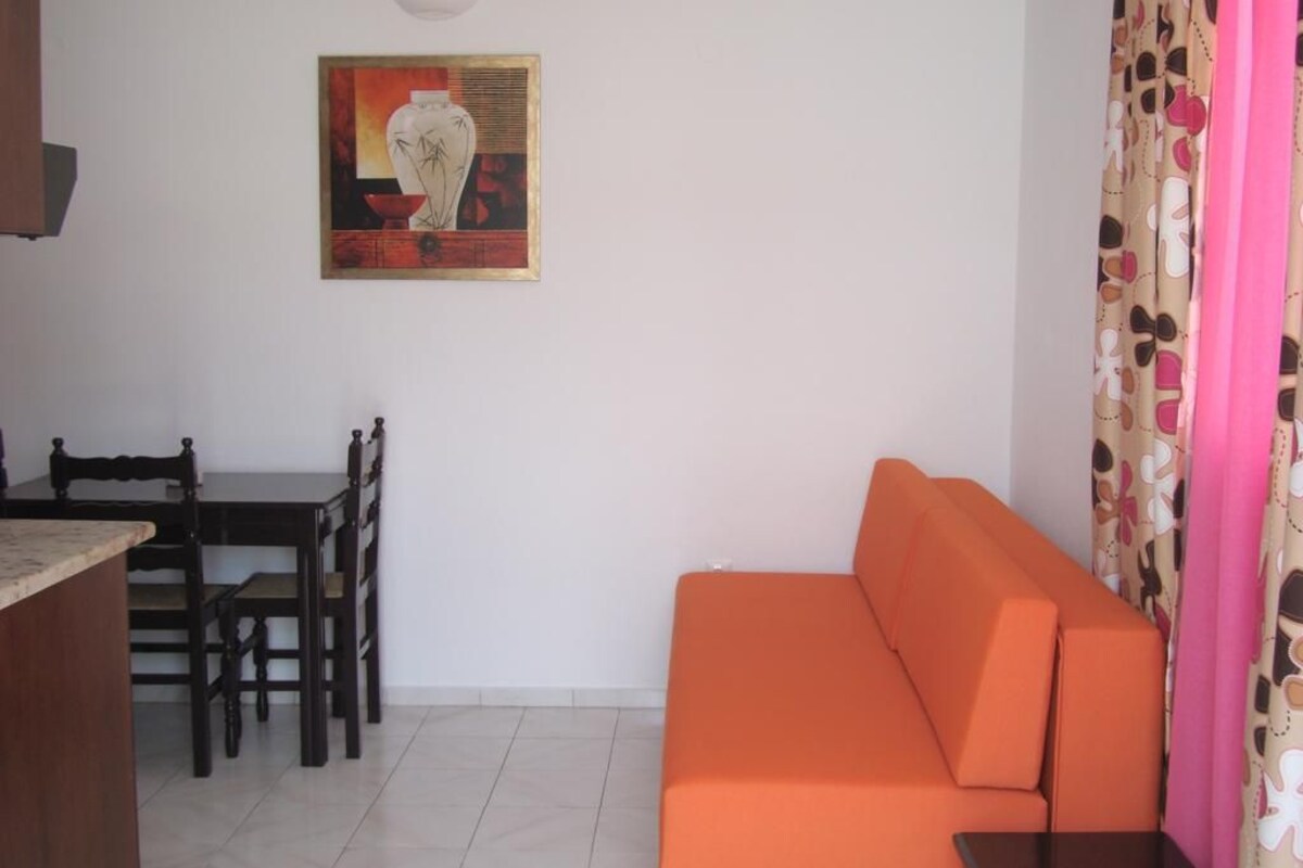 A living room with a sofa, a dining table with chairs, and a painting on the wall.