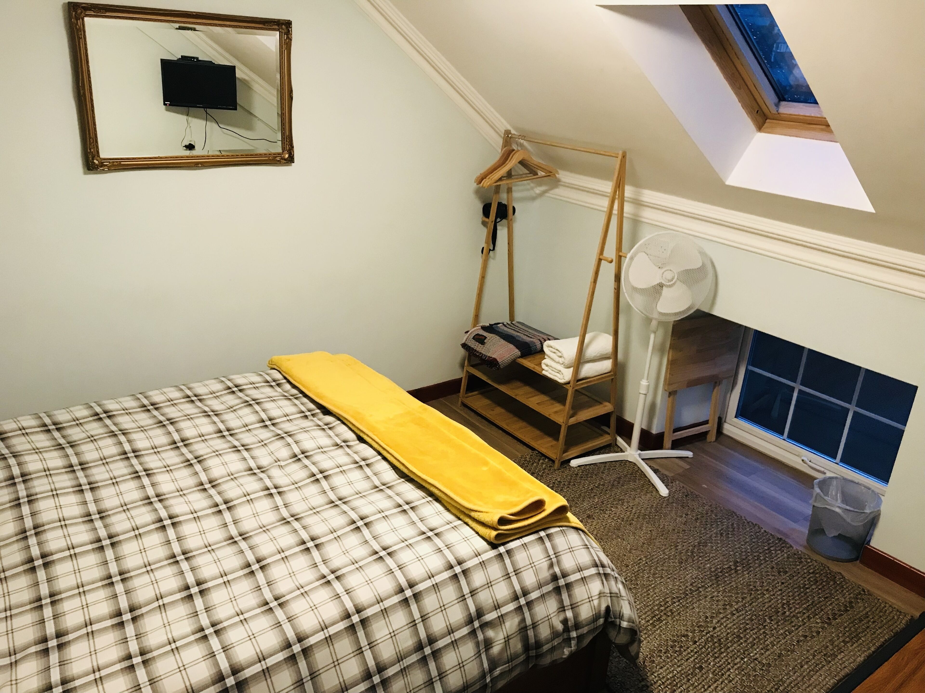 A bedroom with a bed, a wooden wardrobe, a hanging chair, a fan, and a skylight.