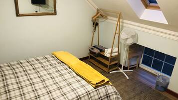 A bedroom with a bed, a wooden wardrobe, a hanging chair, a fan, and a skylight.