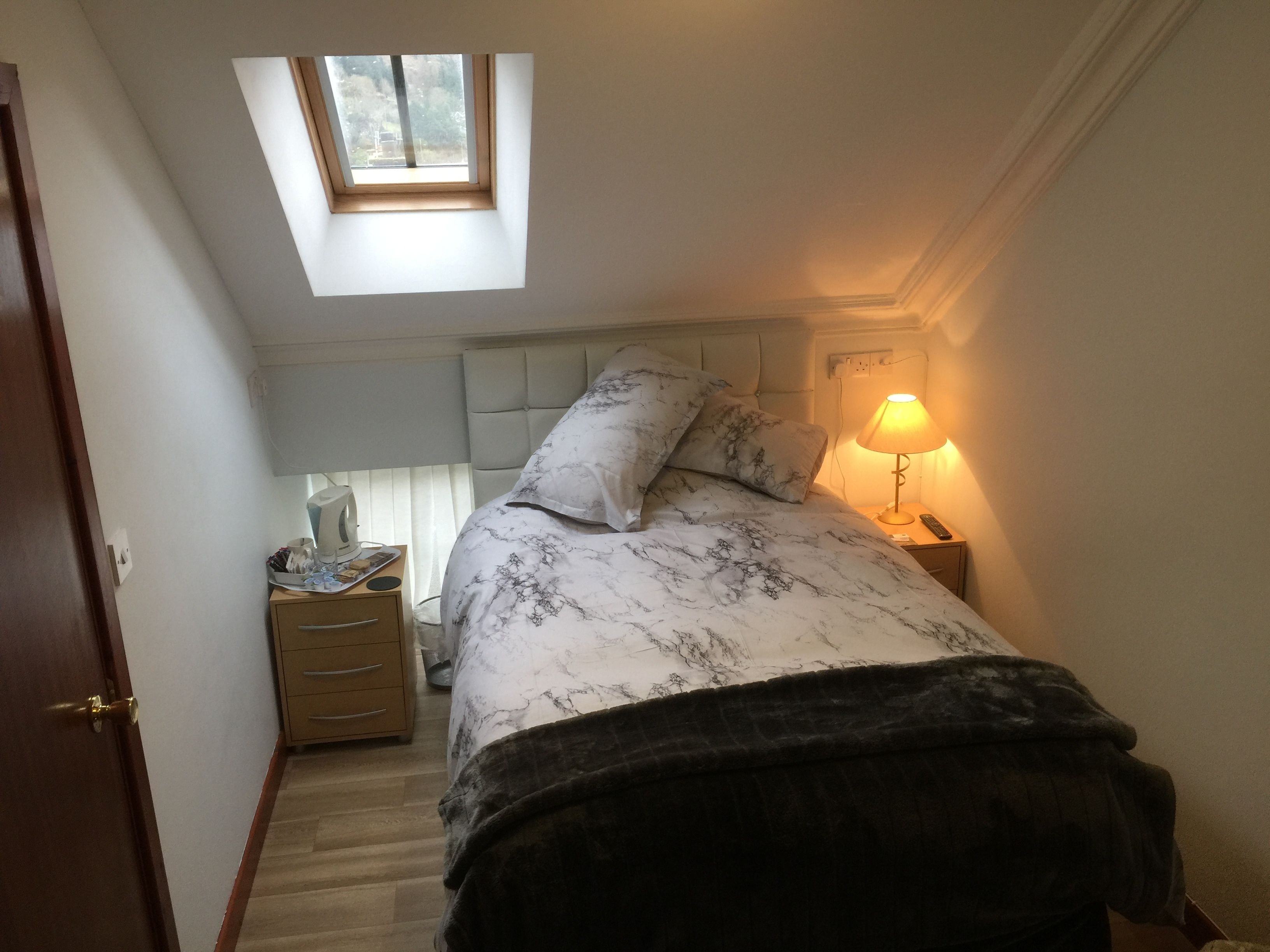 Un dormitorio con tragaluz, una cama con cubrecama estampado en mármol, una lámpara de noche y una mesita de noche de madera.