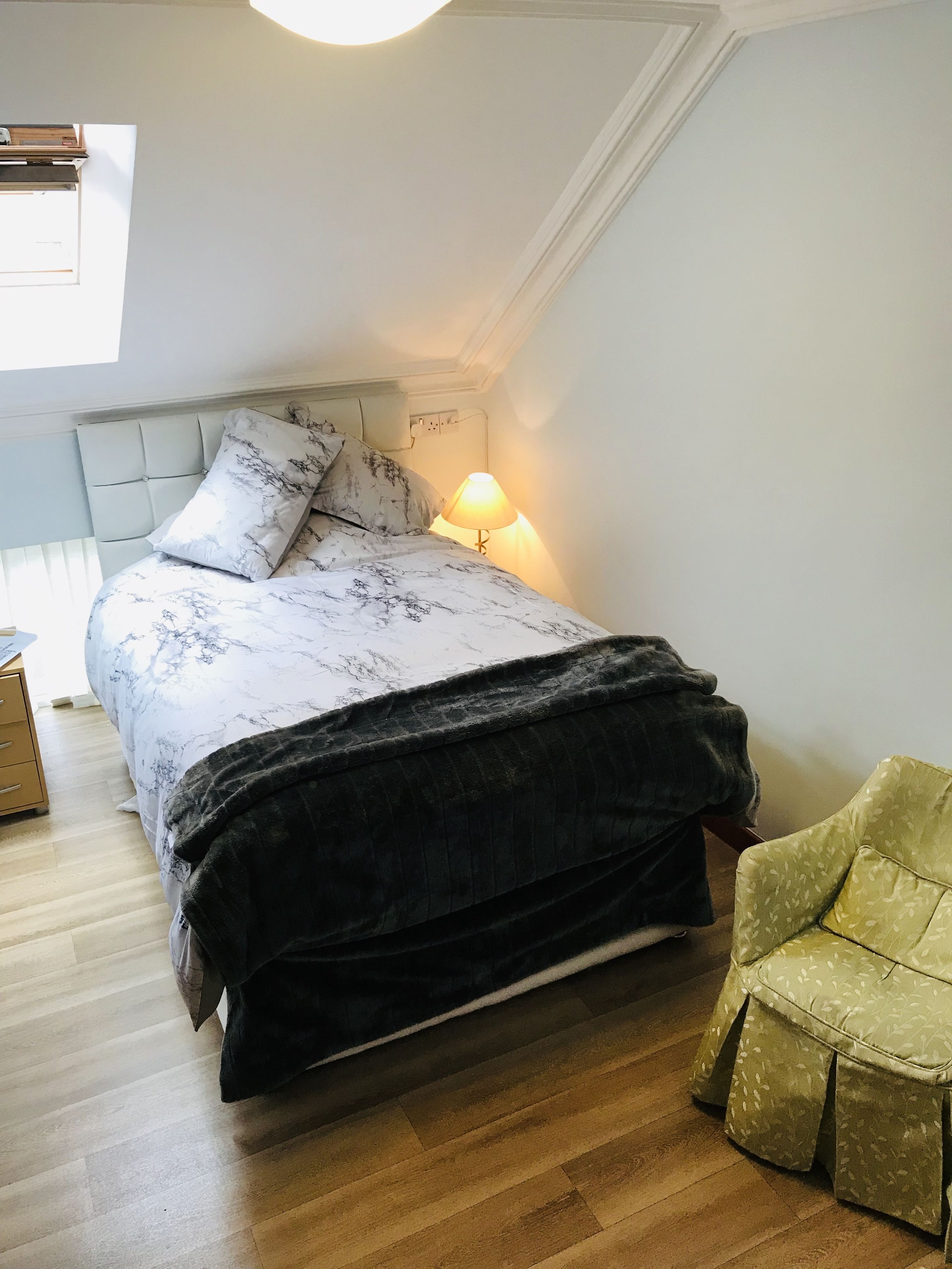A bedroom with a bed, a bedside lamp, a chair, and a window.