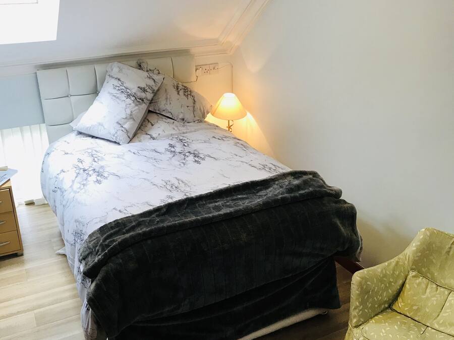 A bedroom with a bed, a bedside lamp, a chair, and a window.