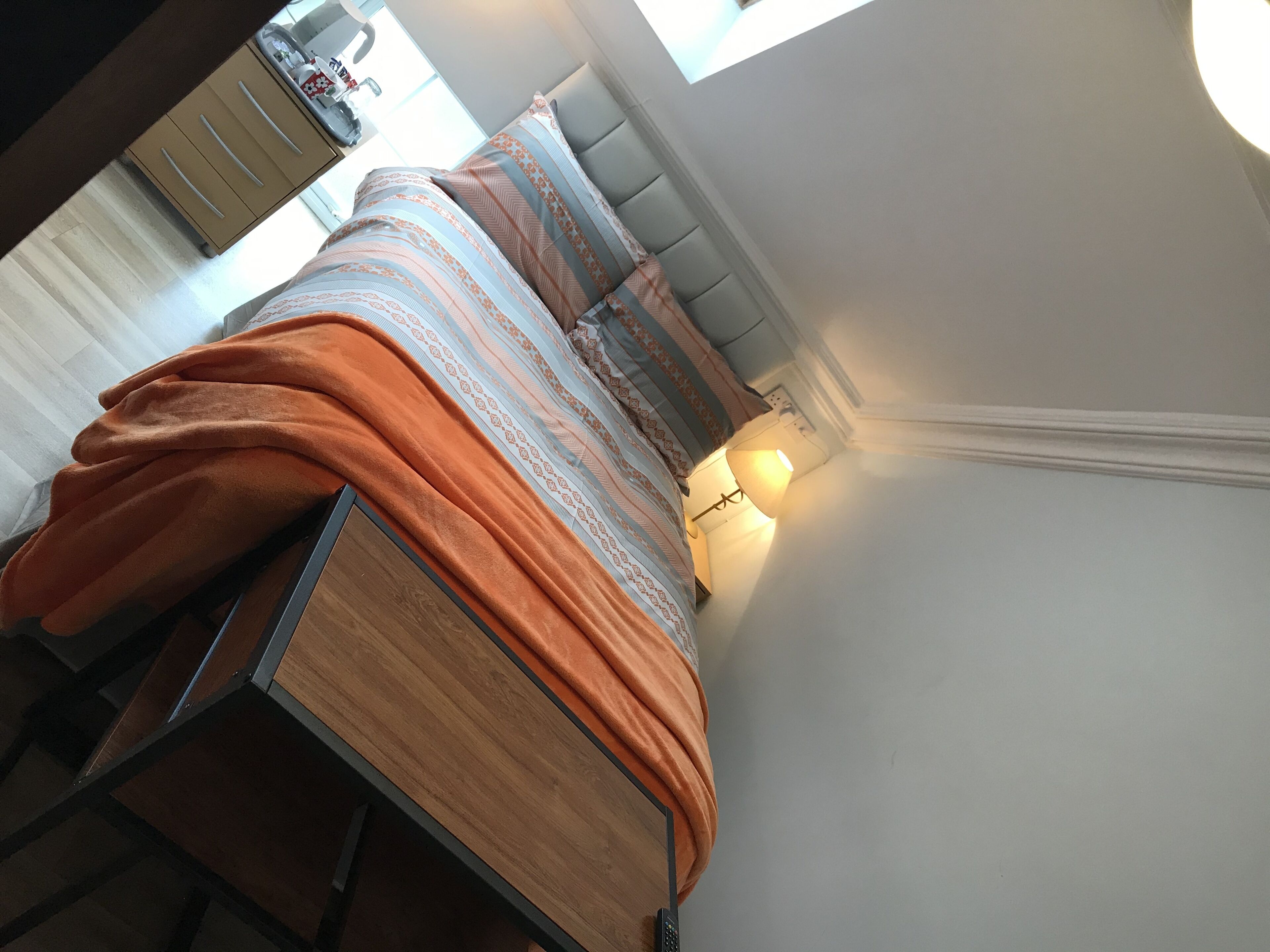 A neatly made bed with an orange blanket, a bedside lamp, and a window with curtains.