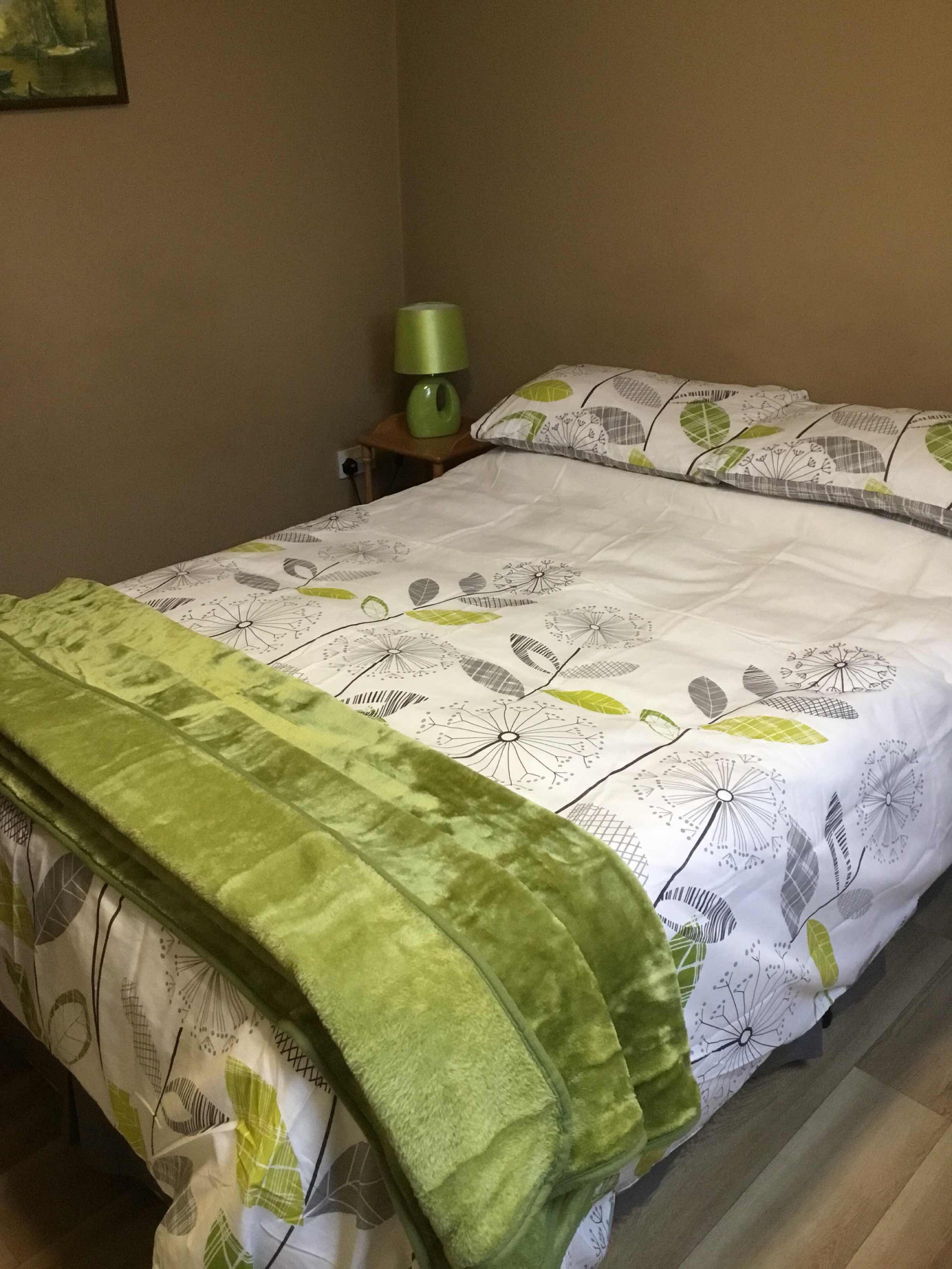 Una cama bien hecha con una manta verde y ropa de cama estampada con motivos florales.