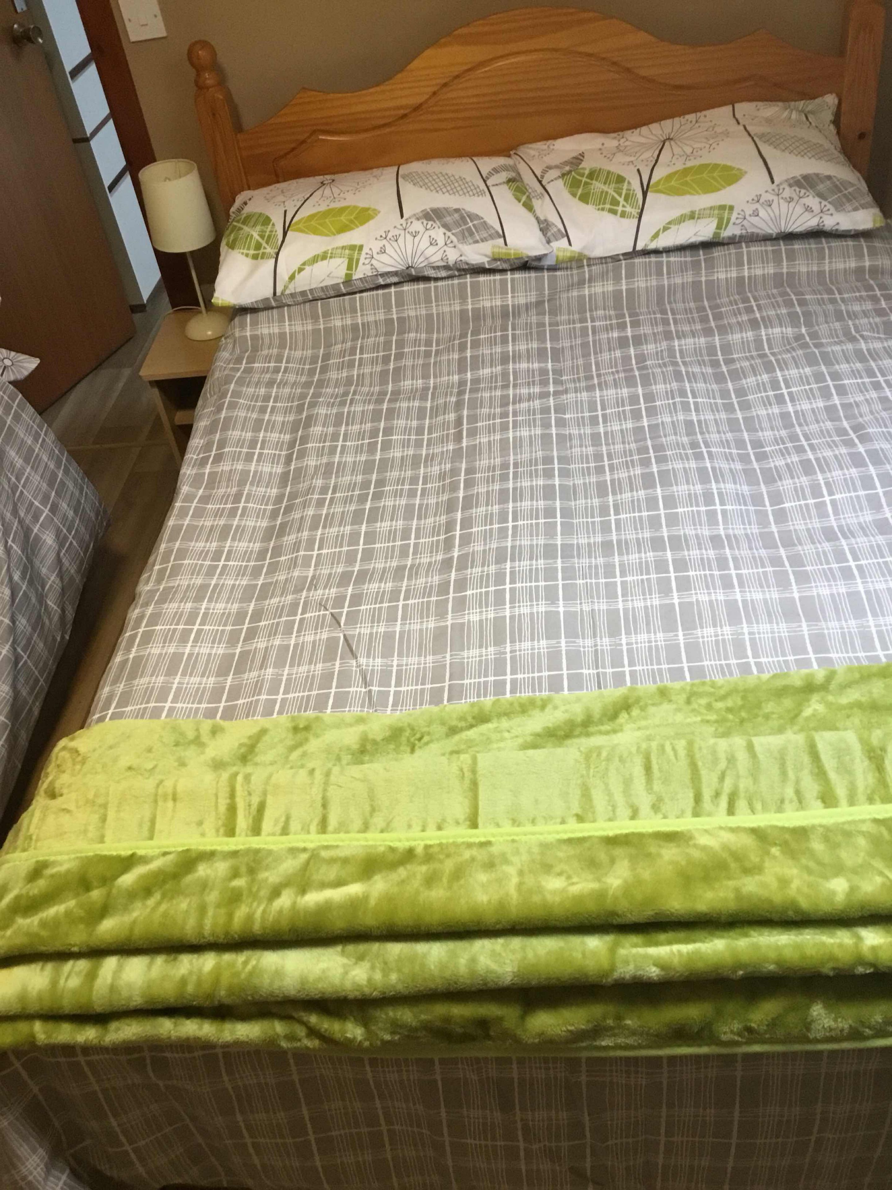 A bed with a grey and white checkered bedspread, a green blanket, and a wooden headboard.