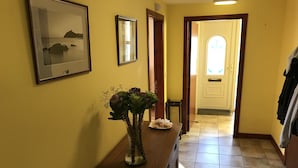 A hallway with a wooden console table, a vase with flowers, framed pictures on the wall, and a door at the end. - Pisgah Guest House Snowdonia (Blaenau Ffestiniog)