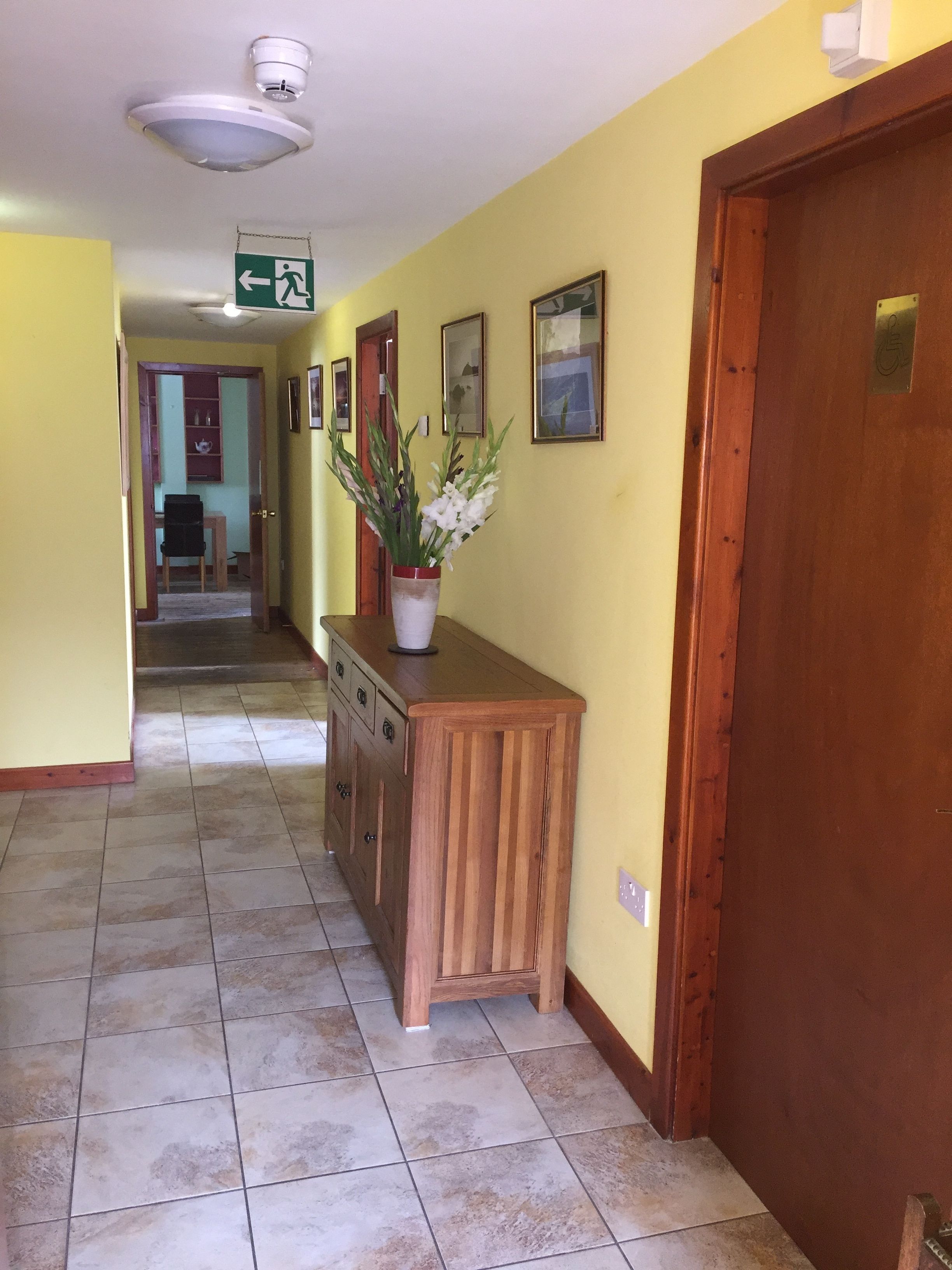 A hallway with a wooden bench, a potted plant, and a door with a plaque.