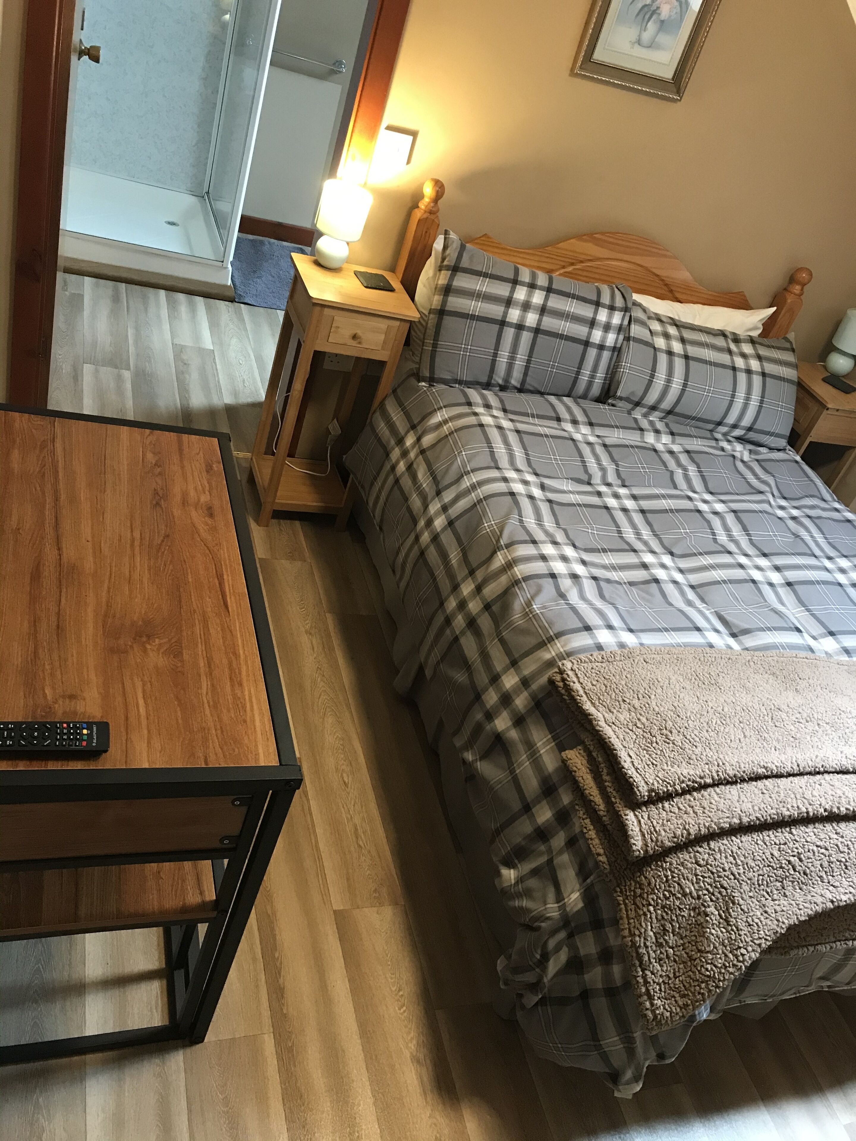 A bedroom with a bed, a nightstand, a bedside lamp, a wooden table, and a remote control.