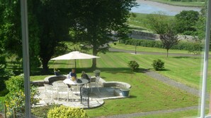 A patio with outdoor seating and a view of a well-maintained lawn and distant water body. - Fludha Guest House (Kirkcudbright)