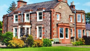A stone building with multiple chimneys, a green lawn, and a bench. - Fludha Guest House (Kirkcudbright)