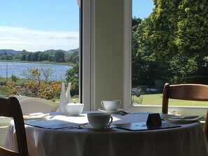 A dining table with a view of a lake and greenery. - Fludha Guest House (Kirkcudbright)