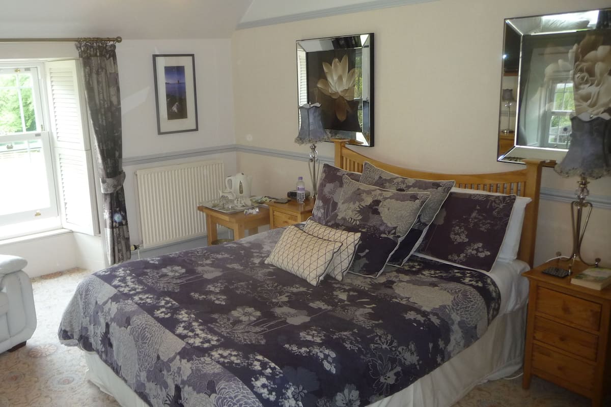 A bedroom with a large bed, a bedside table, a chair, and a window with curtains.