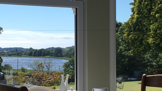A table set for two with a view of a lake and greenery. - Fludha Guest House (Kirkcudbright)