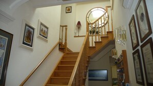 A wooden staircase with a handrail, leading to a landing with a mirror and framed pictures on the walls. - Fludha Guest House (Kirkcudbright)
