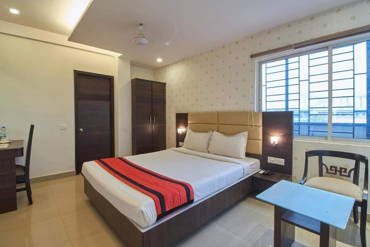 A hotel room with a bed, a desk, a chair, and a window with blinds.