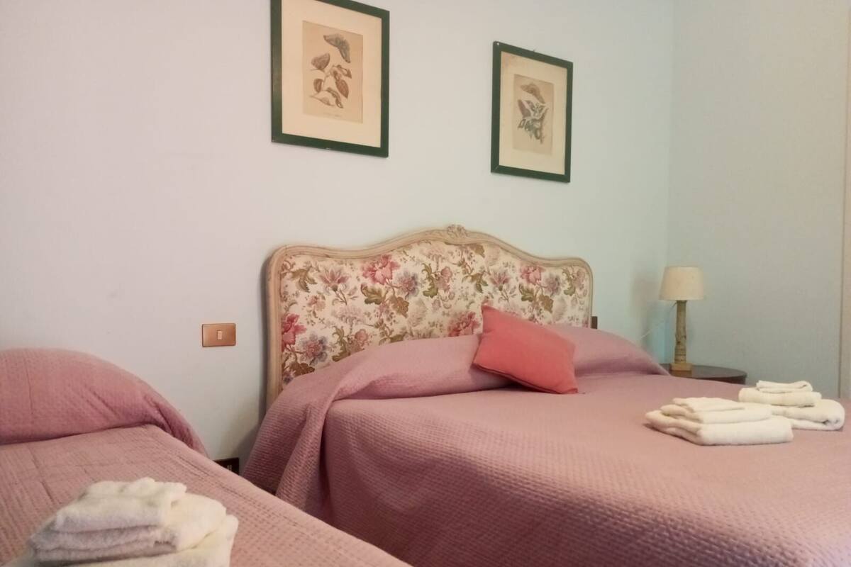 A bedroom with two beds, floral headboards, pink bedding, and a nightstand with a lamp.