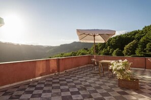 A checkered terrace with a table and chairs, an umbrella, and a potted plant. - Agriturismo Cerrolungo (La Spezia)
