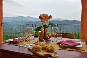 A table set for two with a vase of a single rose, two wine glasses, and a plate of food, overlooking a mountainous landscape. - Agriturismo Cerrolungo (La Spezia)
