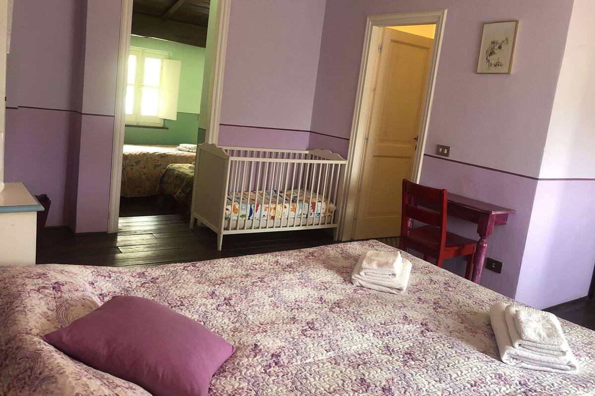 A room with a bed, a crib, a chair, and a door leading to another room.