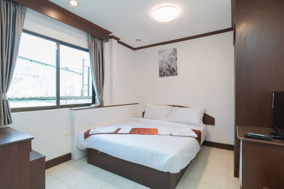 Une chambre d’hôtel avec un lit, un bureau, une fenêtre avec des rideaux et un tableau au mur.