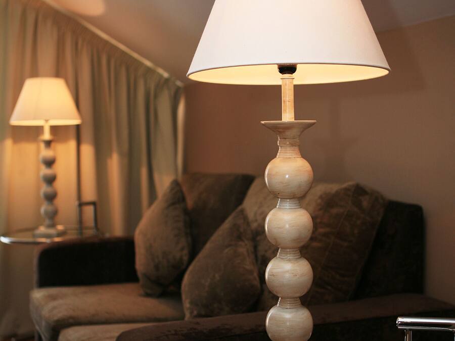 A lamp with a white shade on a round table, a box of chocolates, and a sofa in the background.