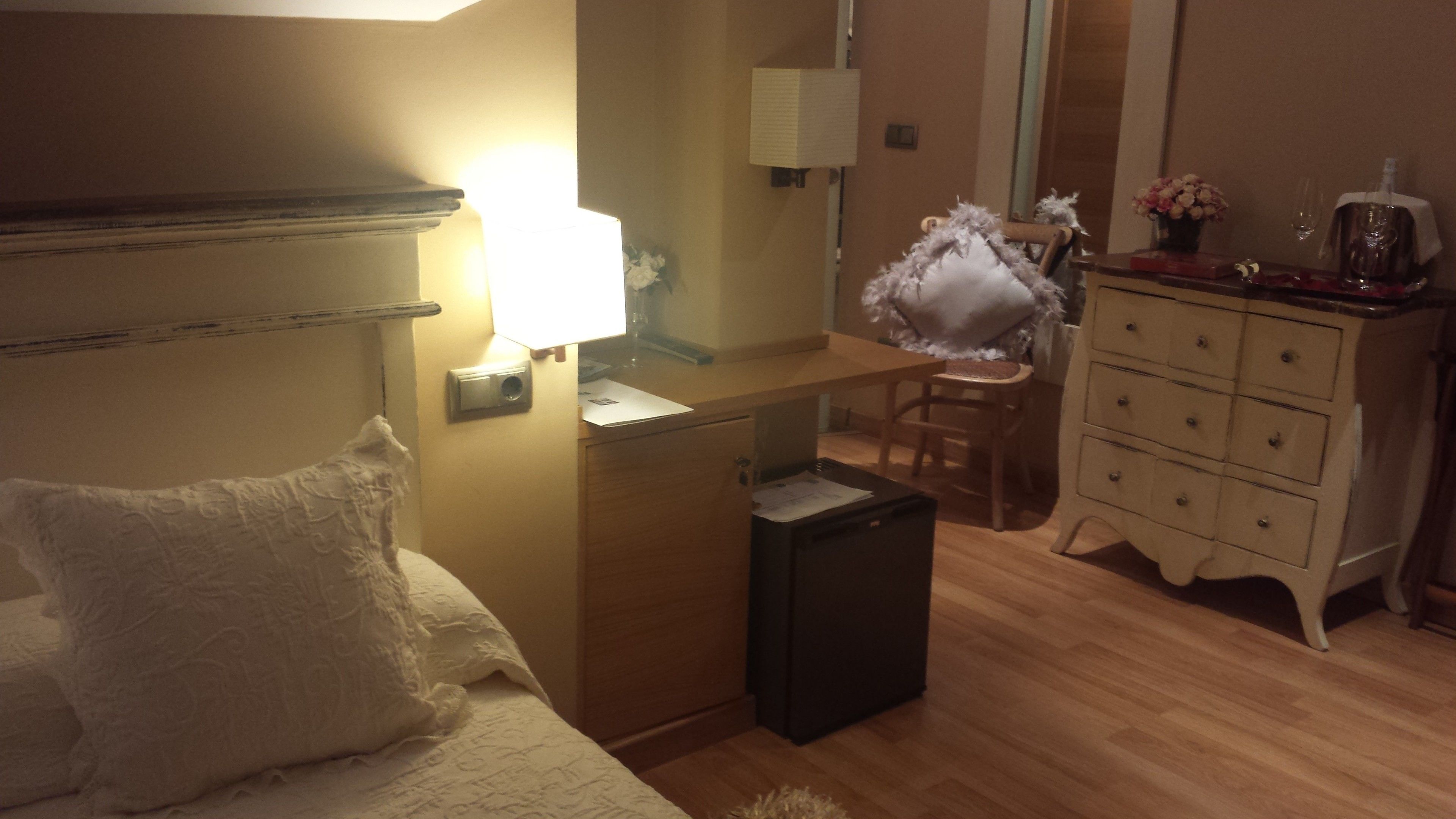 A hotel room with a bed, a desk with a lamp, a dresser, and a trash bin.