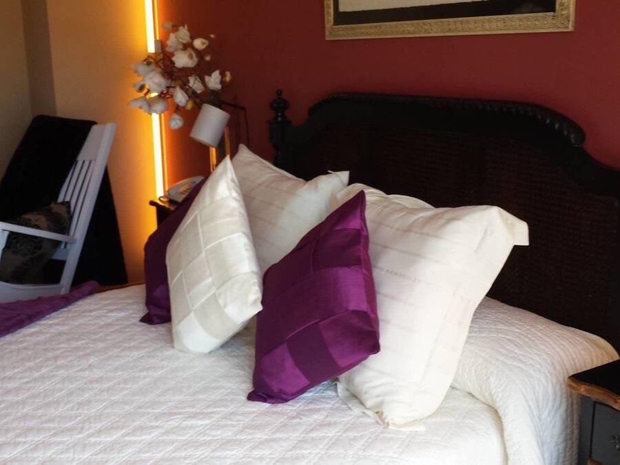 A bed with white and purple pillows, a bedside table with a candle, and a chair in the corner.