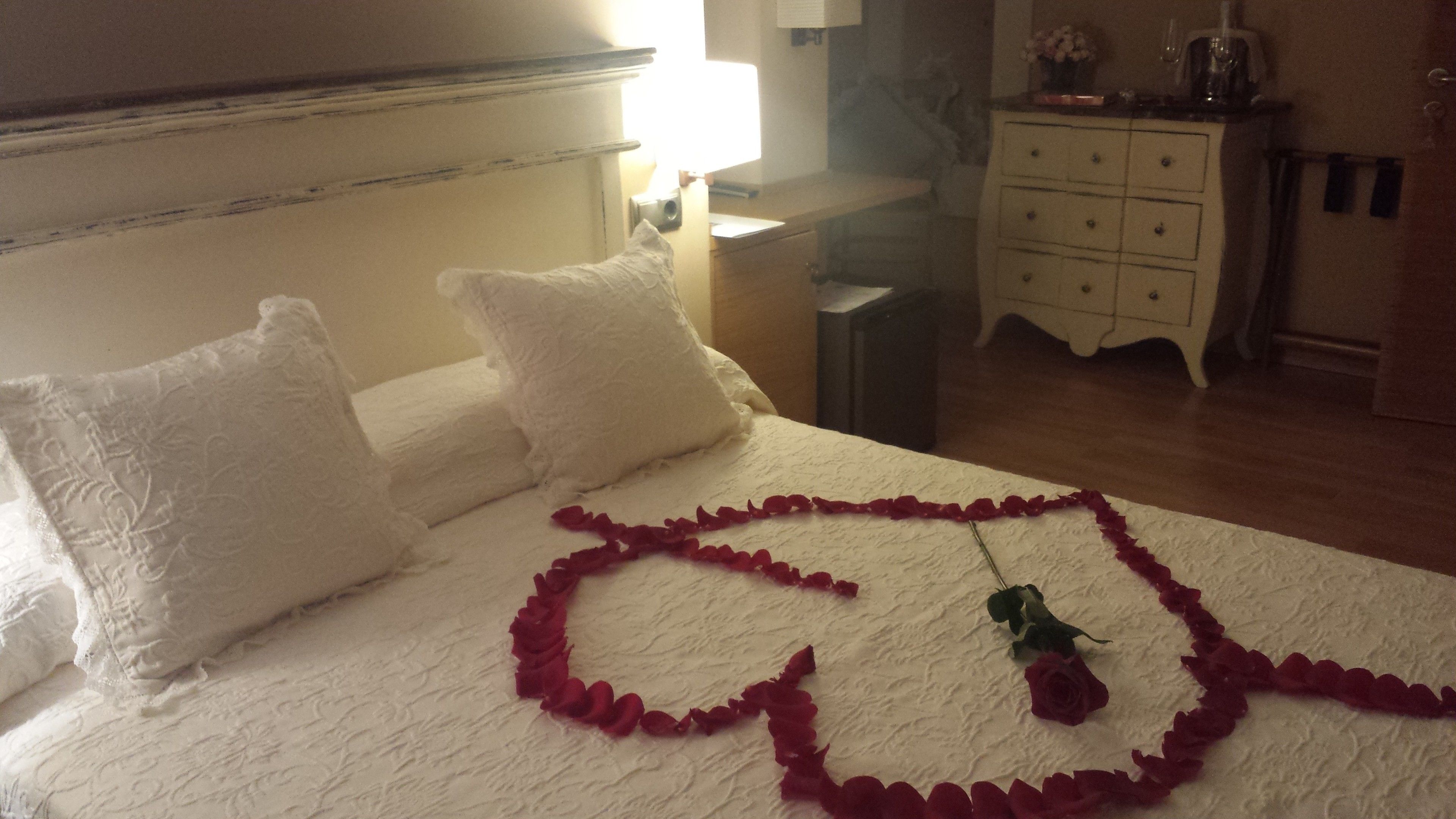 A hotel room with a bed, pillows, a bedside table, a lamp, a dresser, and a mirror.