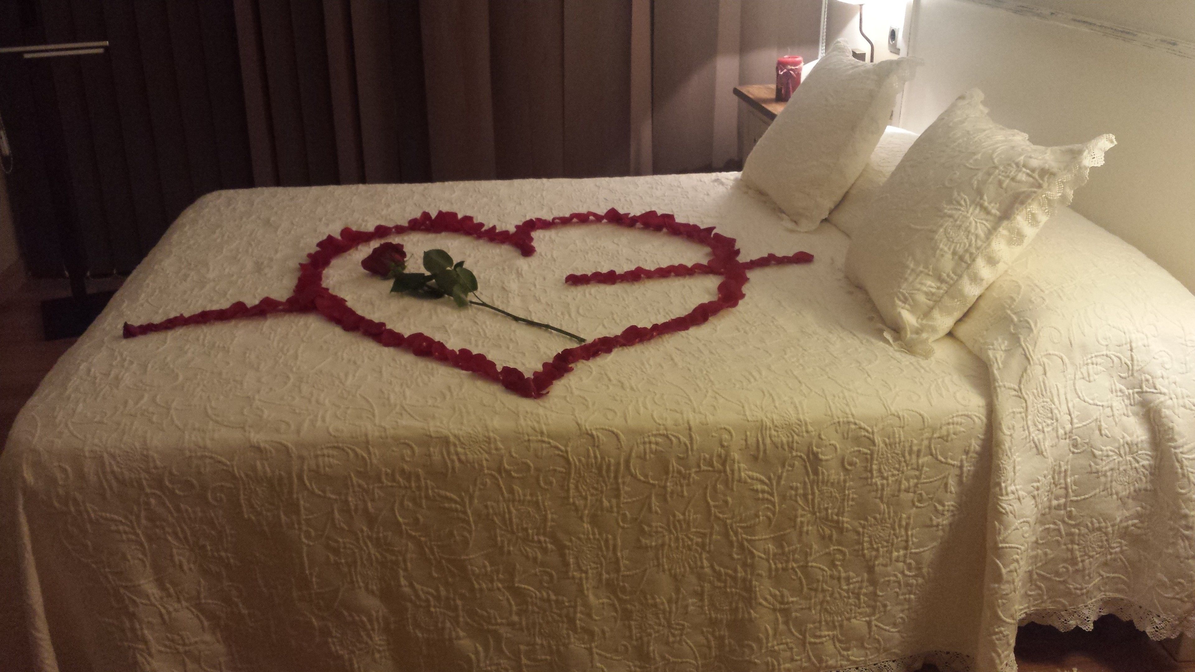 Una cama con una decoración en forma de corazón hecha de pétalos de rosa y una sola rosa.