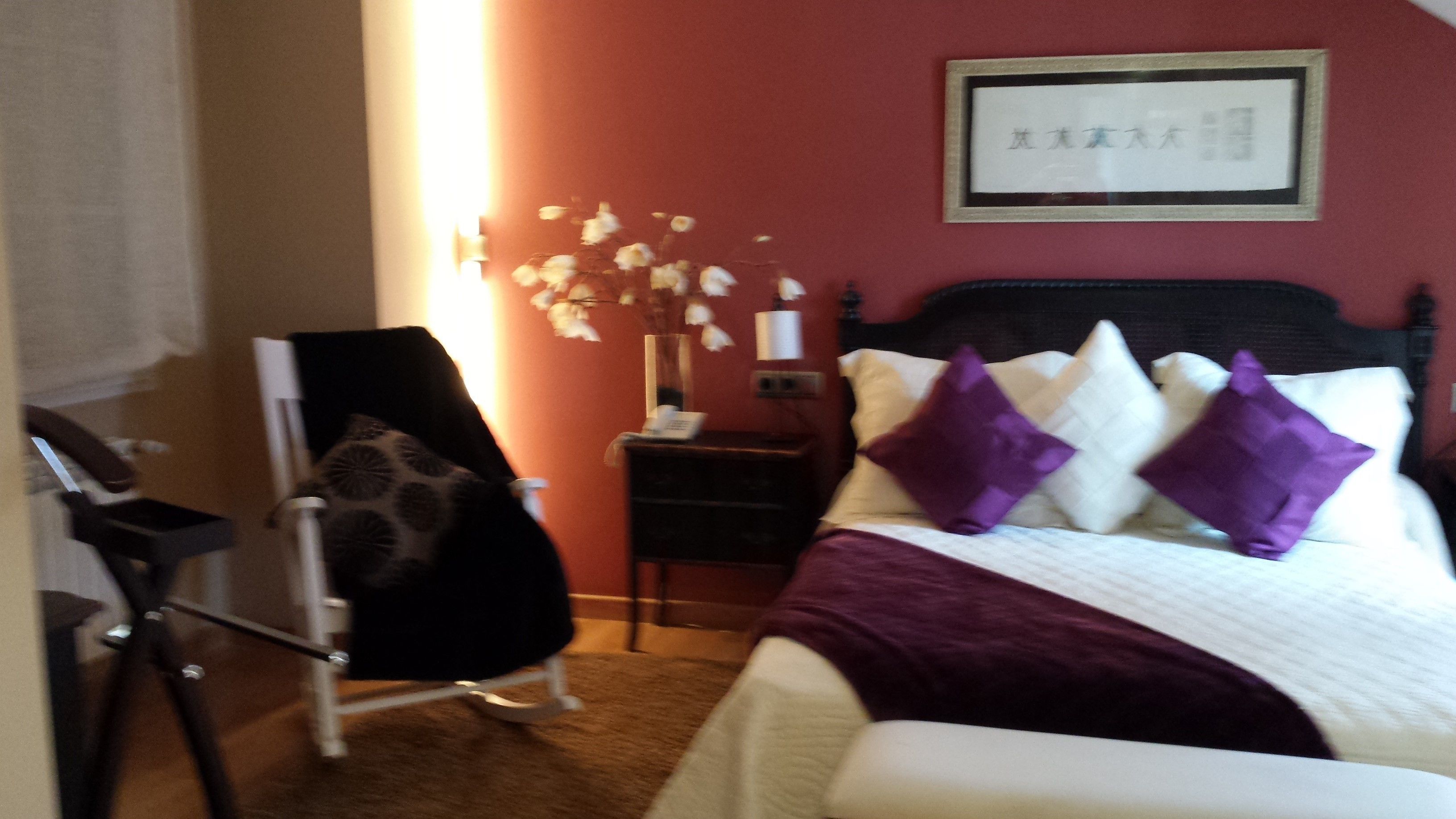 A hotel room with a bed, a nightstand, a chair, and a wall-mounted light fixture.