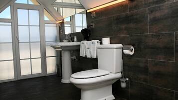 A modern bathroom with a white toilet, dark tiled walls, a window, and a sink with a towel hanging on the wall.