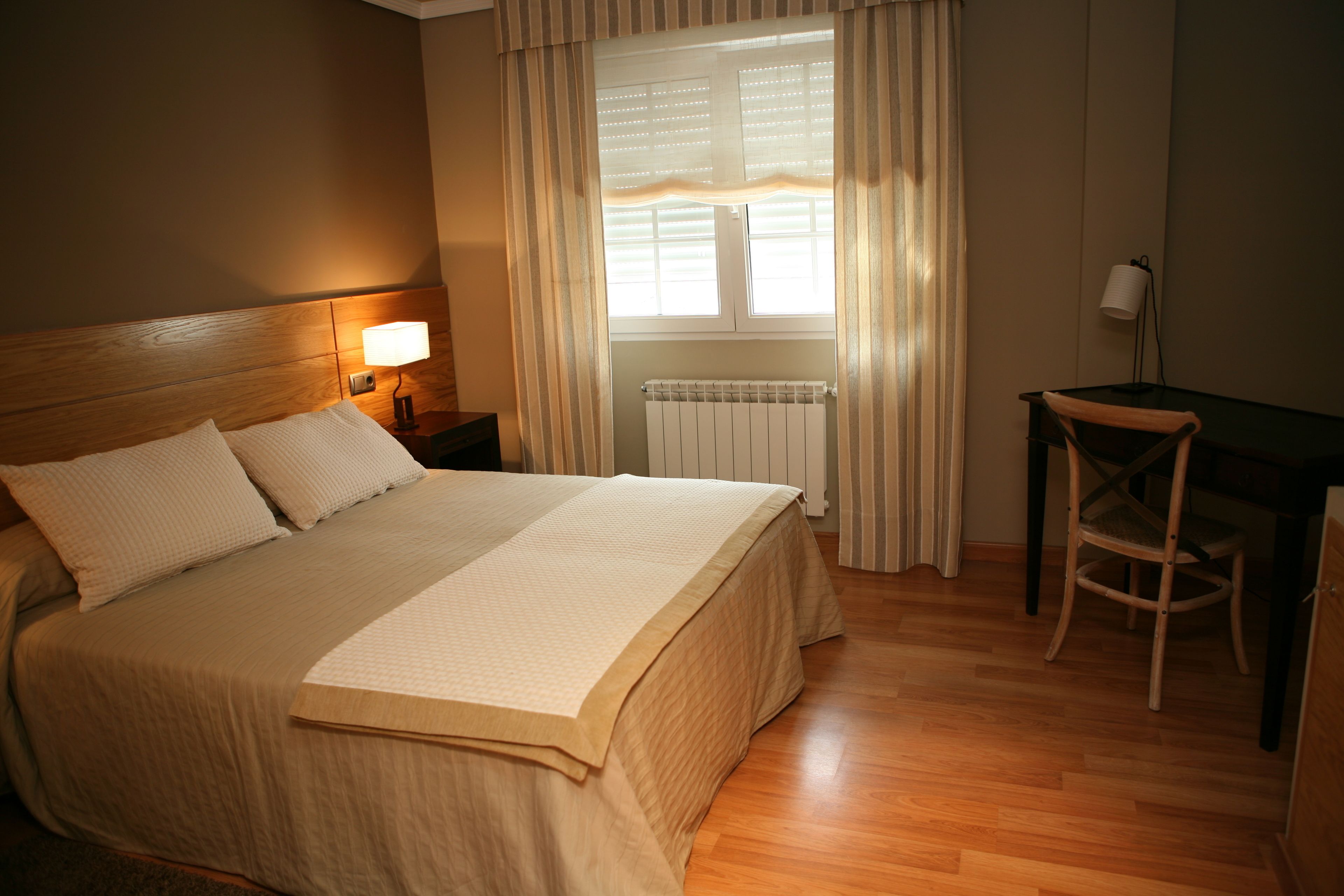 Habitación de hotel ordenada con una cama grande, un escritorio, una silla, un radiador y una ventana con cortinas.