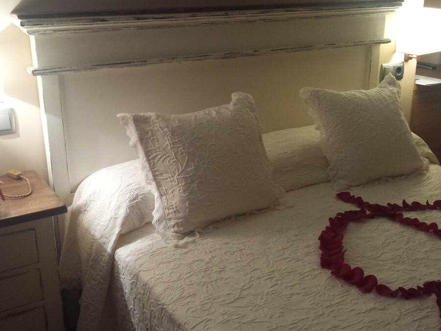 A neatly made bed with white linens and pillows, a bedside table with a lamp, and a decorative rose garland on the bed.