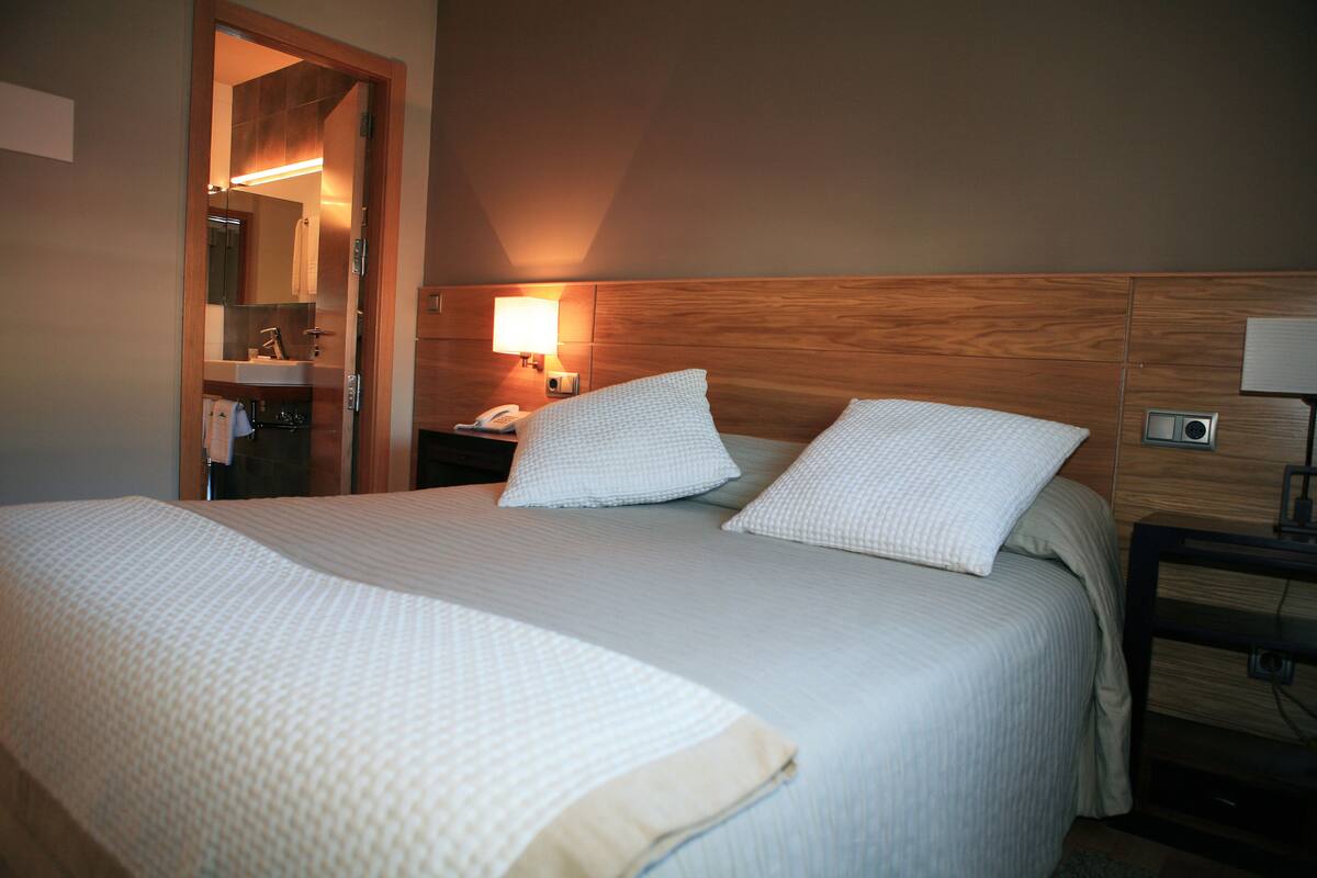 Ein Hotelzimmer mit einem großen Bett, einem Holzkopfteil, einem Nachttisch mit Lampe und einem Spiegel.