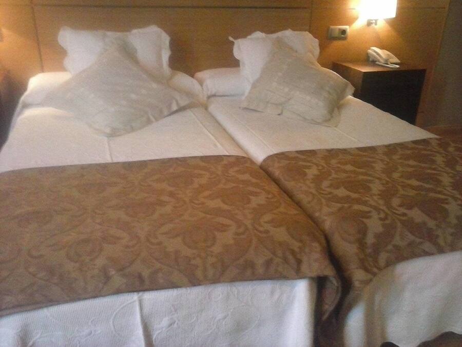 A hotel room with a bed, two pillows, a bedside table with a phone, and a patterned throw blanket.