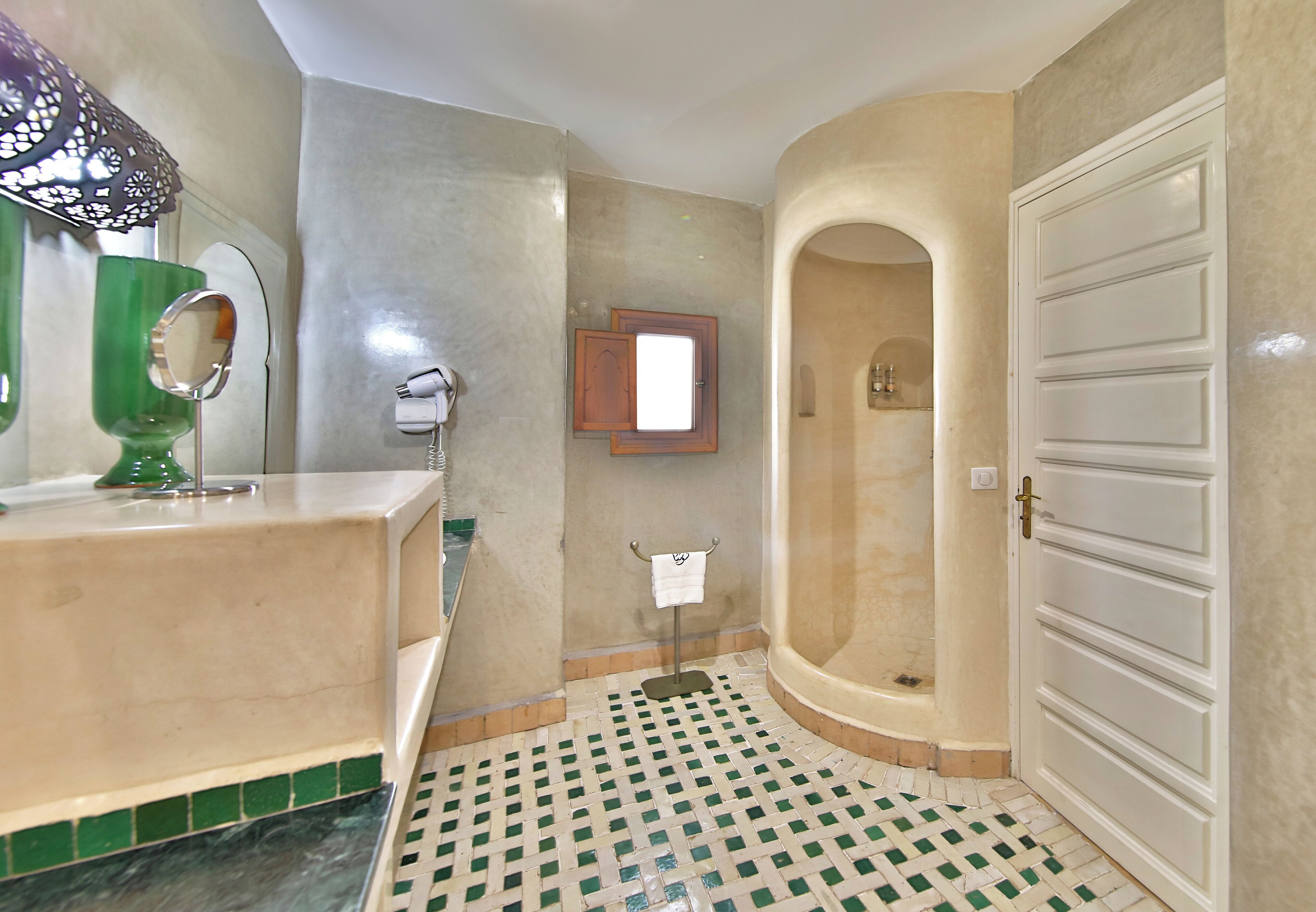 A bathroom with a tiled floor, a sink, a mirror, and a shower area.