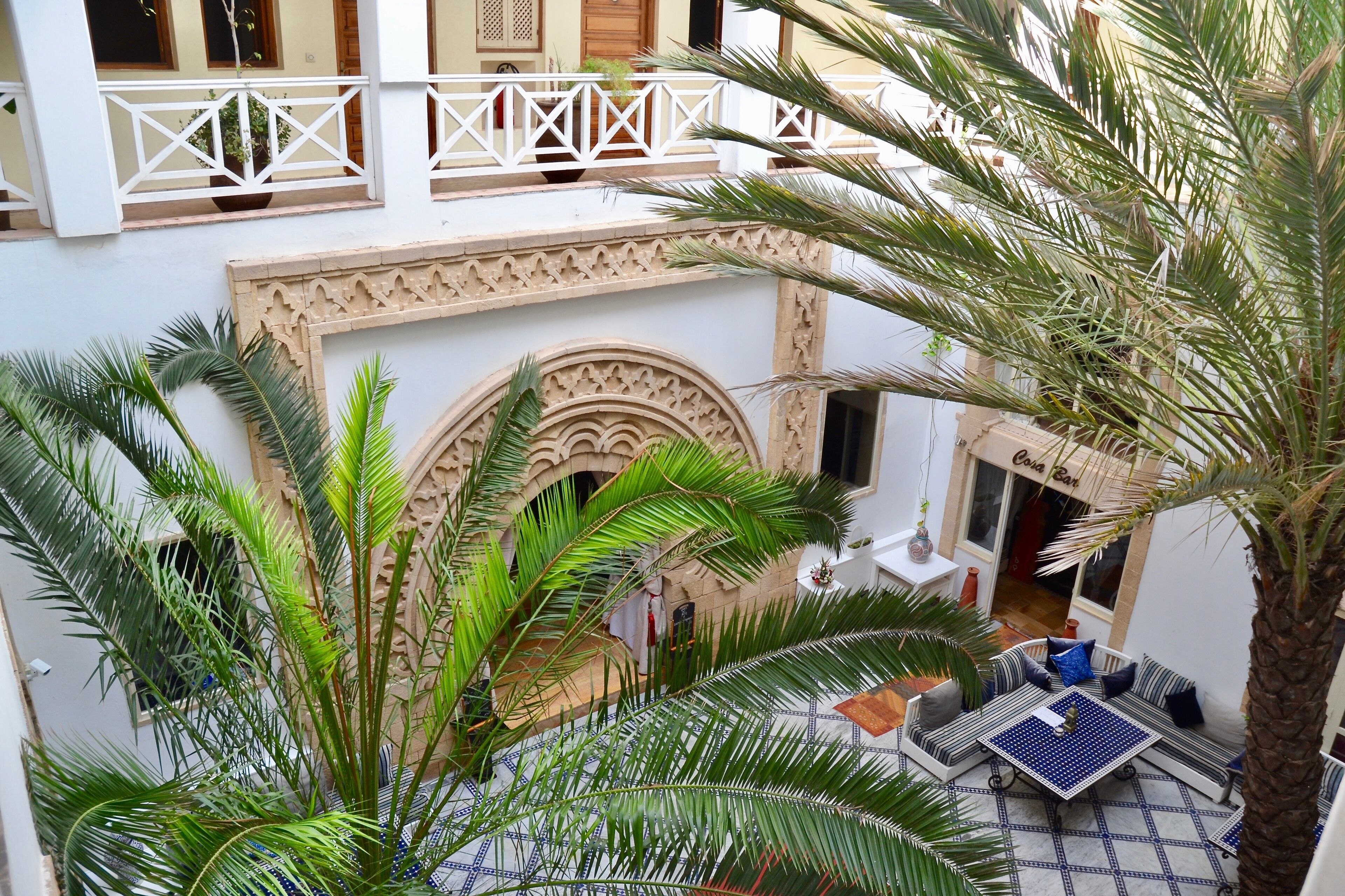 A courtyard with a palm tree, a patterned floor, and a seating area with cushions.