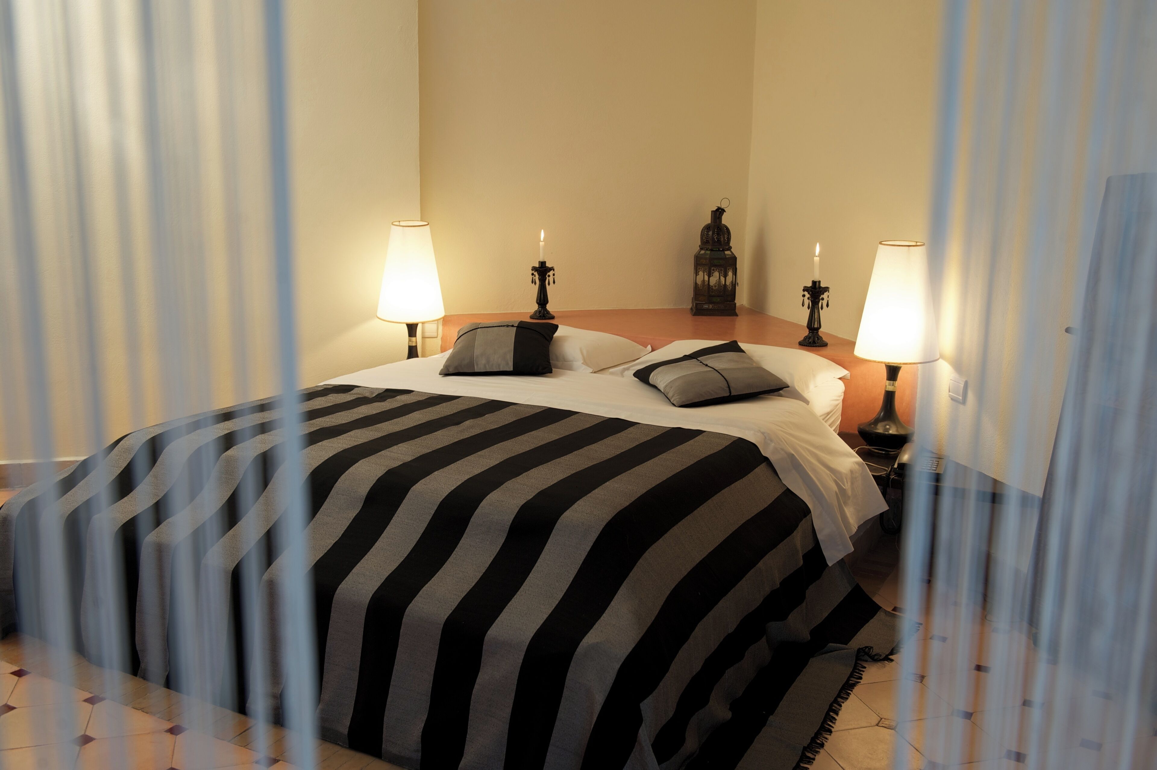A hotel room with a bed, two bedside lamps, a nightstand, a decorative item, and a curtain partially drawn.