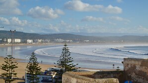 Vista costera con playa, olas del océano y montañas a lo lejos.