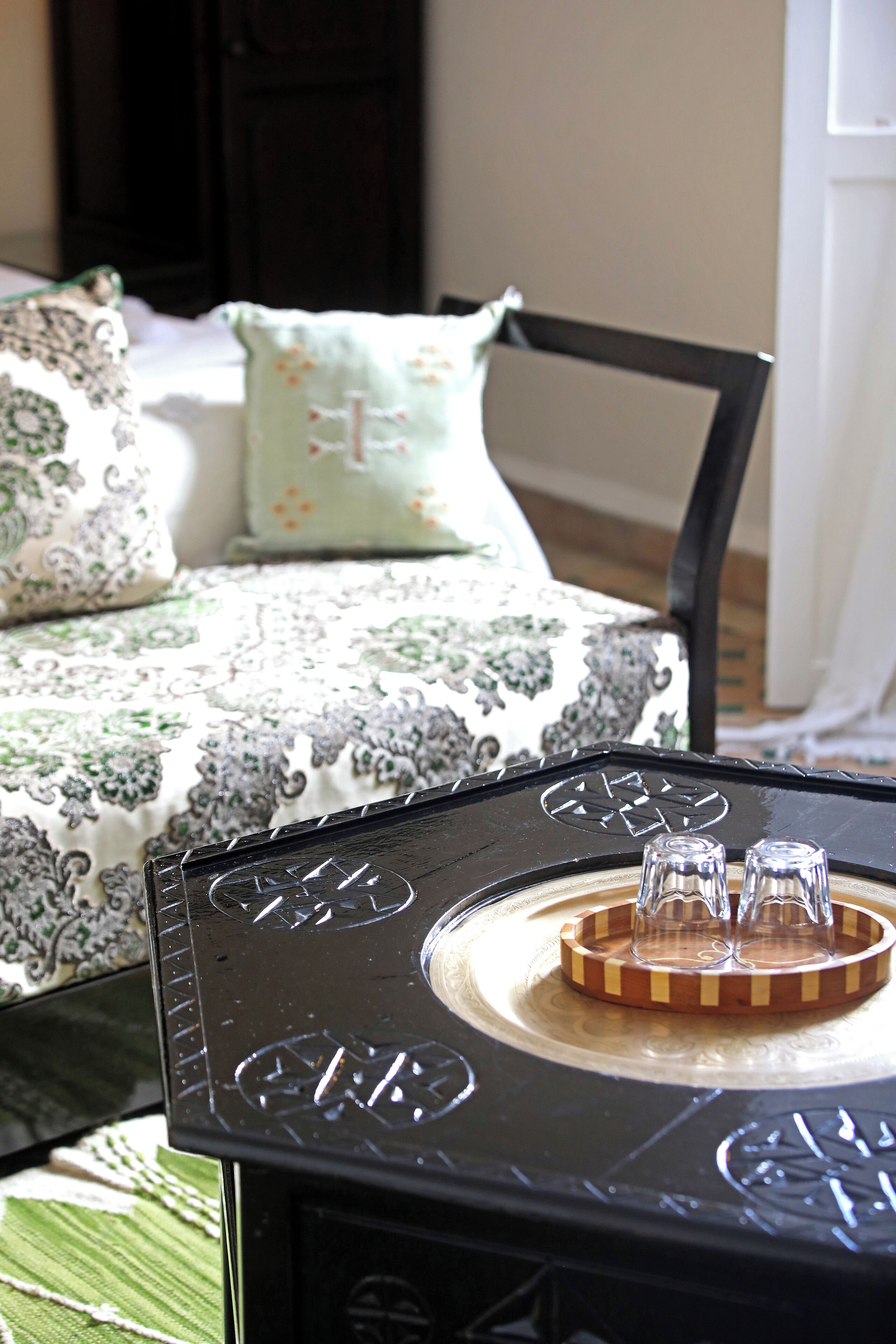 A bed with patterned bedding, a black table with a tray and glasses, and a chair with a dark frame.