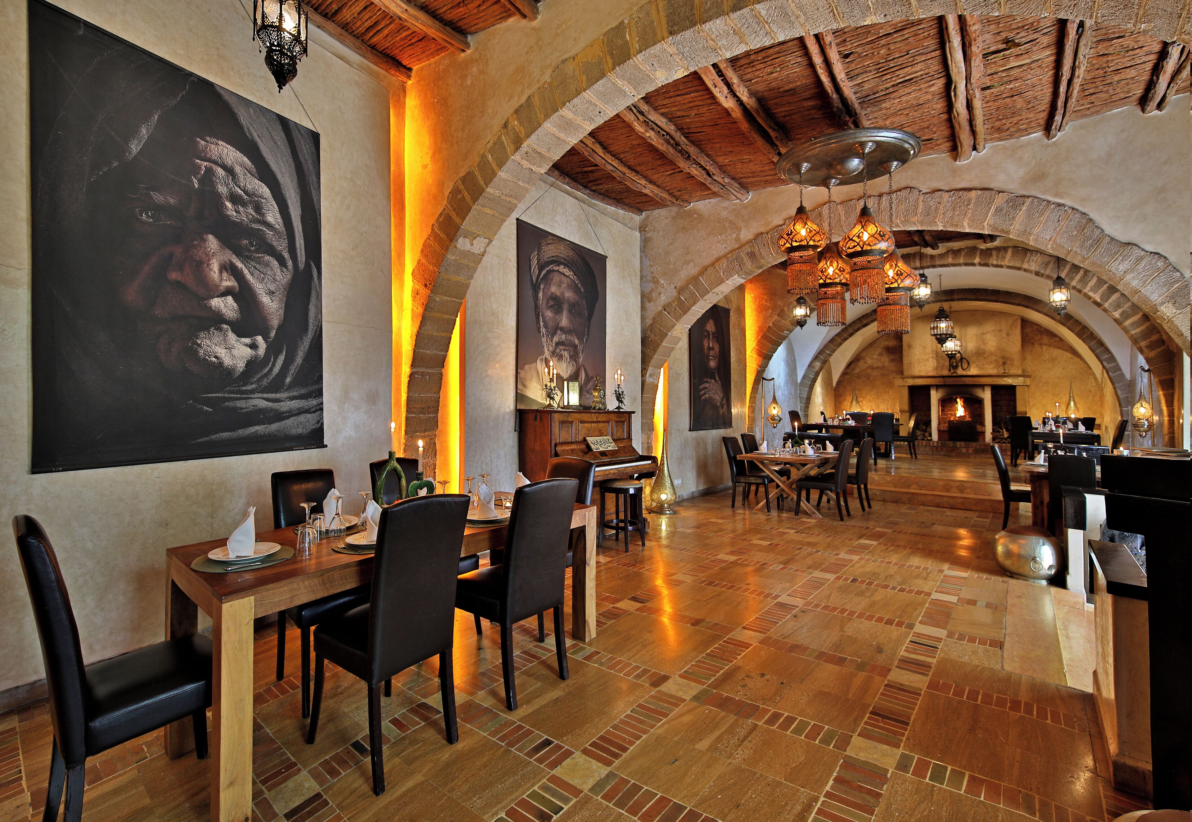 Un restaurante con mesas y sillas de madera, grandes cuadros en las paredes y suelo de ladrillo.