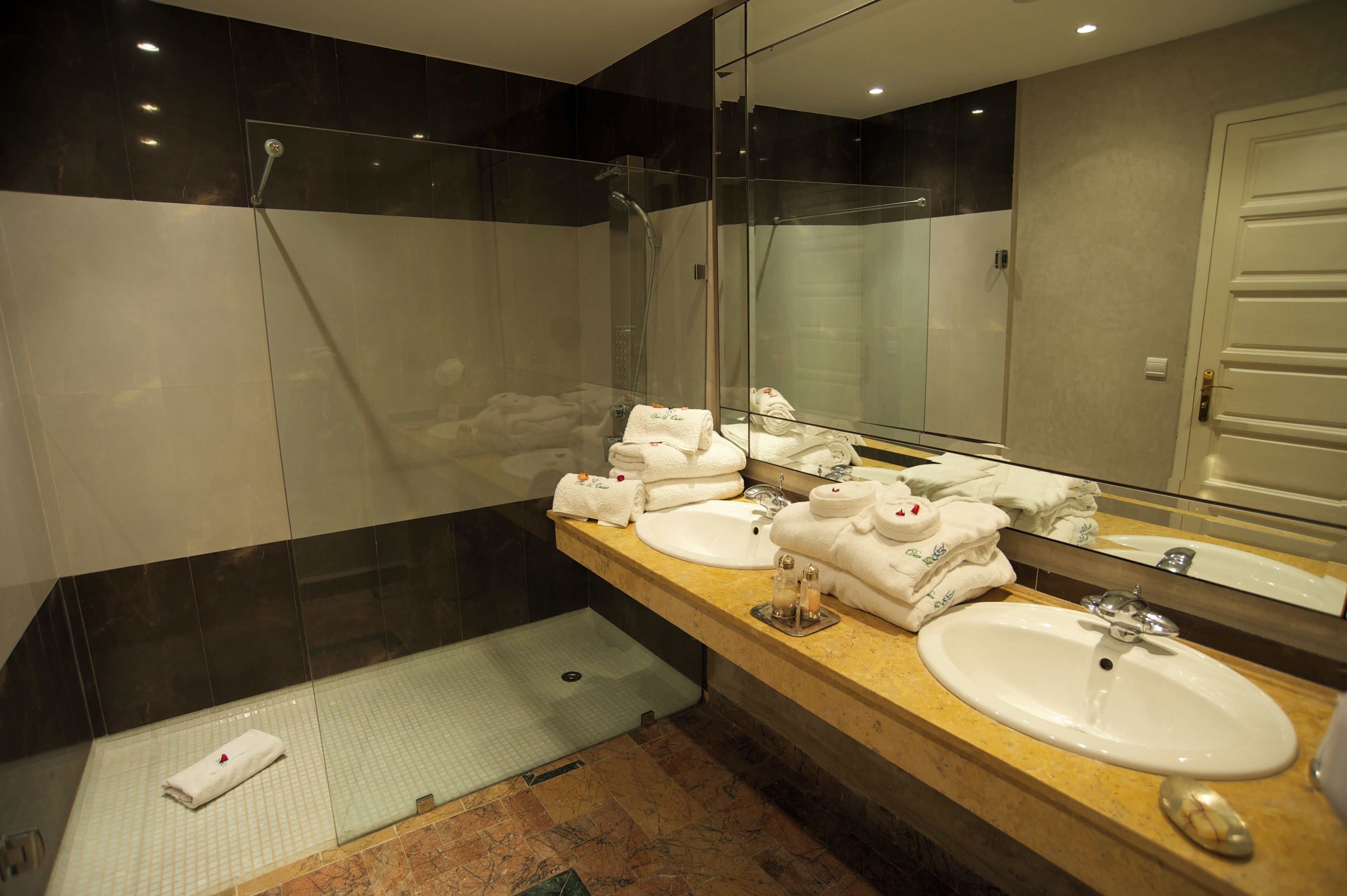 A modern bathroom with two sinks, a glass shower enclosure, and a large mirror.