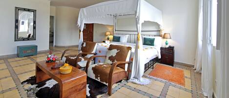 Una habitación con una cama con dosel, una mesita de noche de madera, una alfombra de cuero de vaca y un espejo en la pared.