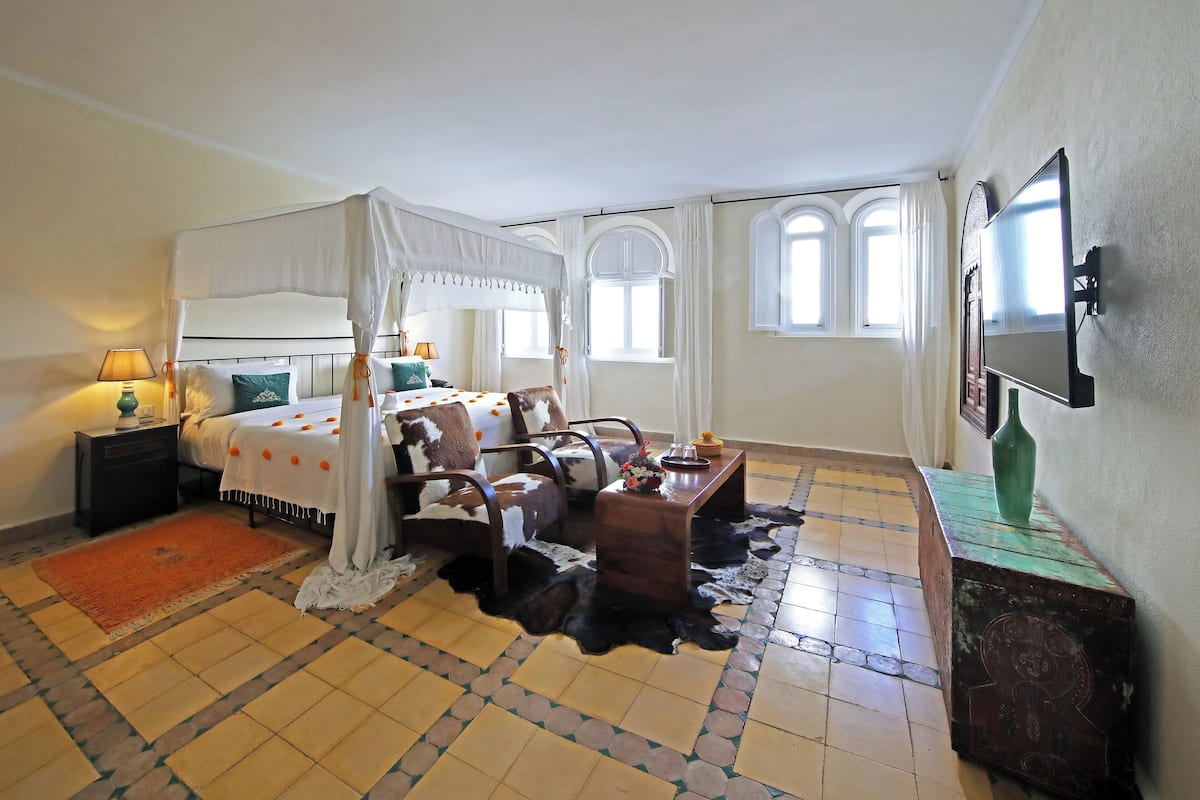 A bedroom with a four-poster bed, a wooden nightstand, a desk with a vase, and a television mounted on the wall.