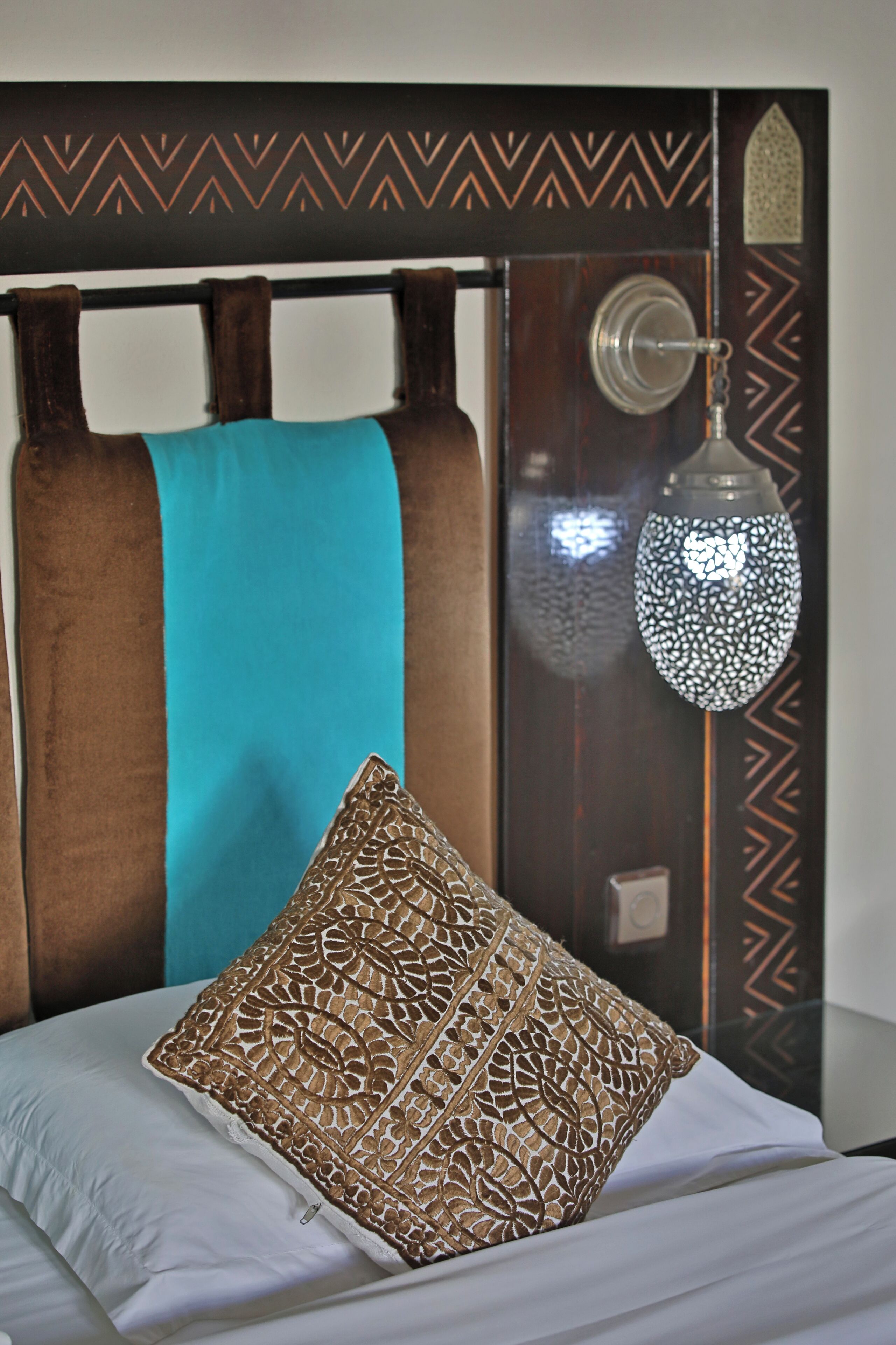 Una cama con un cojín estampado, una manta color turquesa y un panel decorativo en la pared.