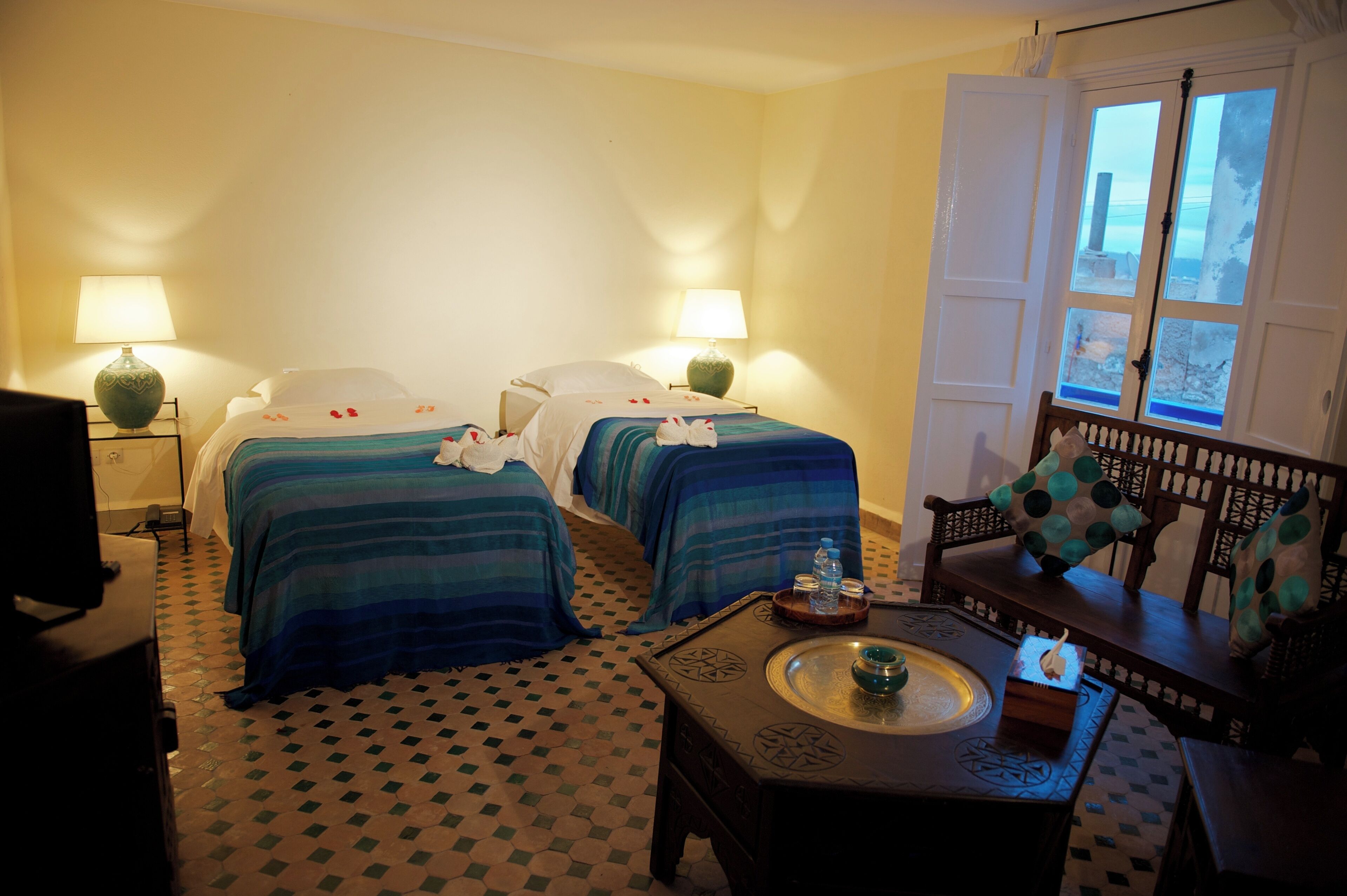A hotel room with two beds, a small table with a tray, a sofa, and a window with a view.