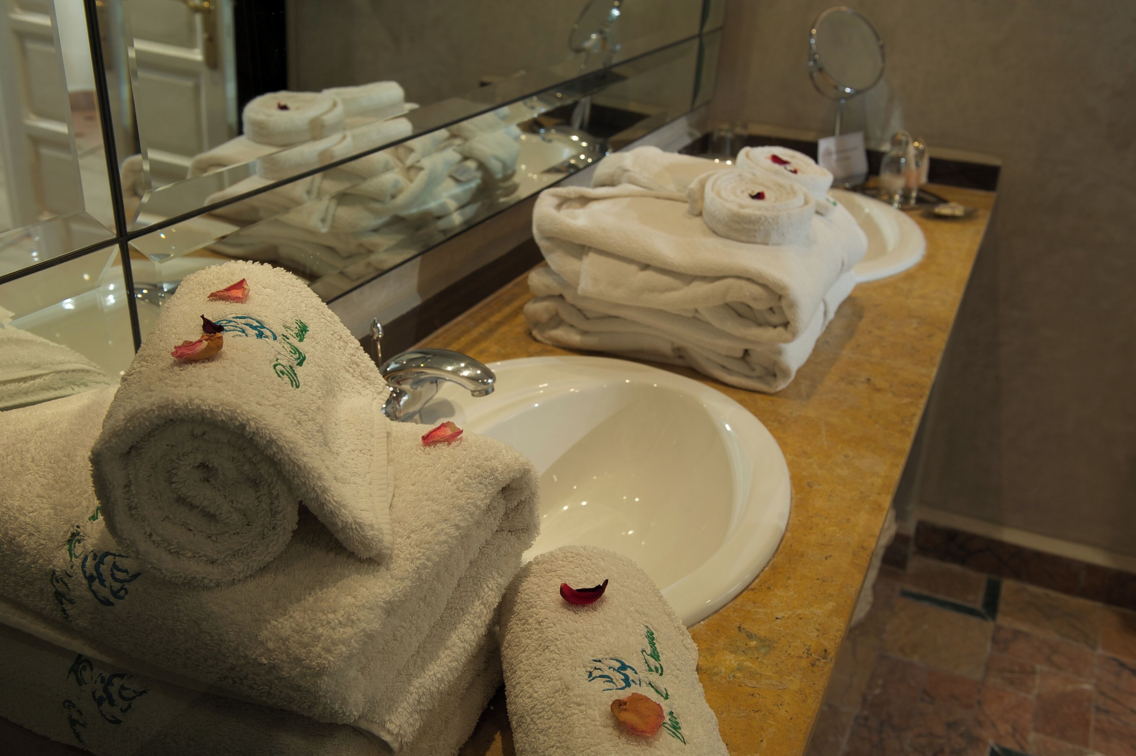 A bathroom with a glass-enclosed vanity, a sink, and a stack of neatly folded towels with floral designs.