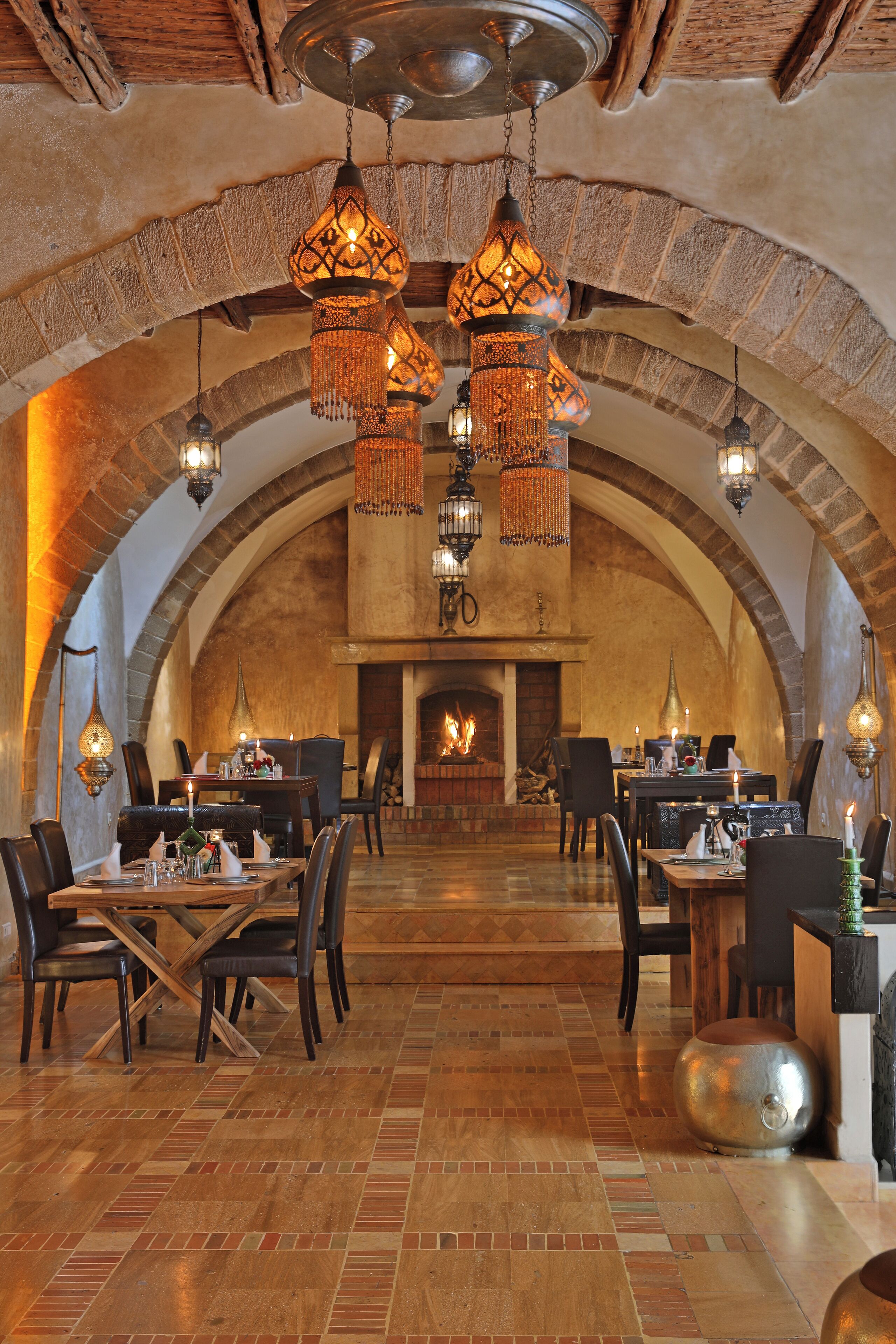 A restaurant with arched brick ceilings, hanging pendant lights, and a fireplace in the background.