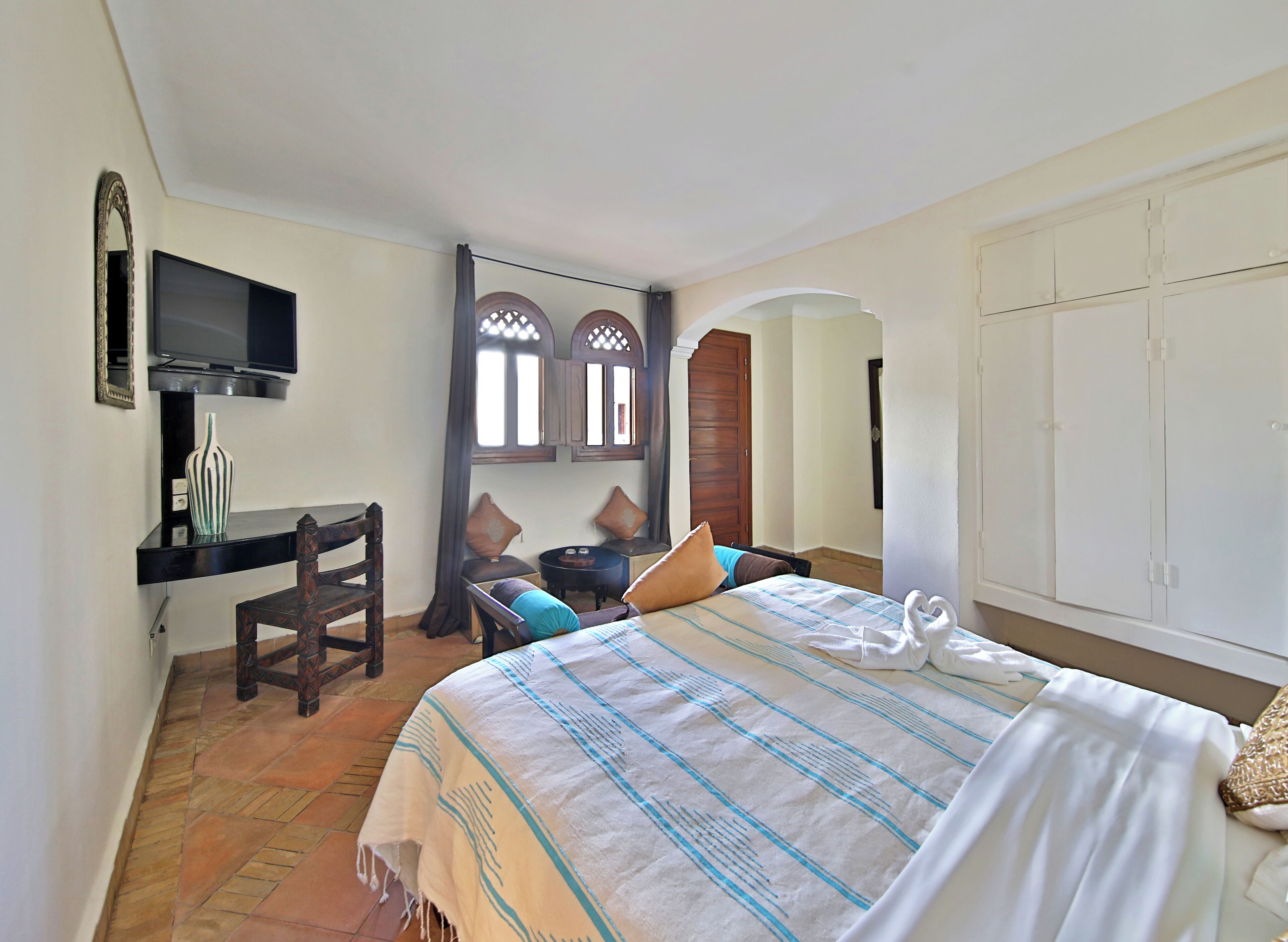 A hotel room with a bed, a desk, a chair, a television, and a wardrobe.