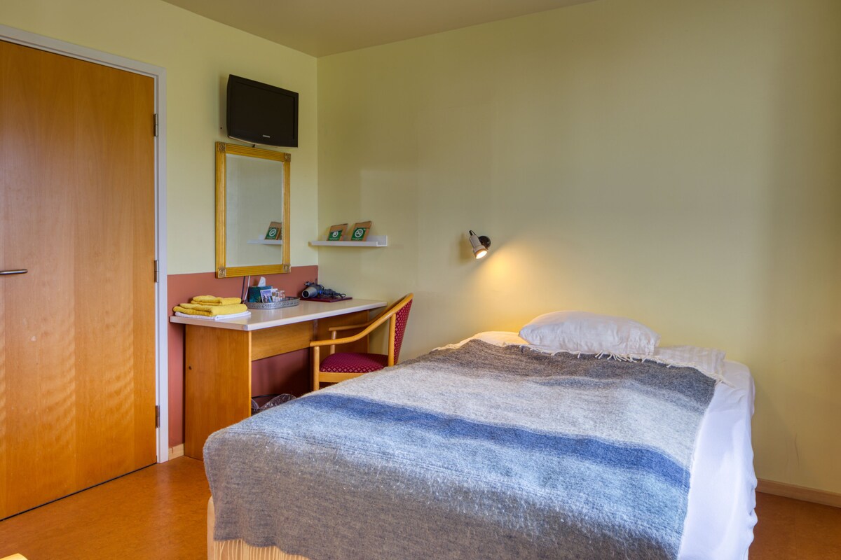 Ein Schlafzimmer mit einem Bett, einem Schreibtisch, einem Stuhl, einem Fernseher und einem Regal mit Gegenständen.